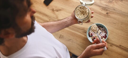 Mann bereitet Müsli mit Haferflocken zu.