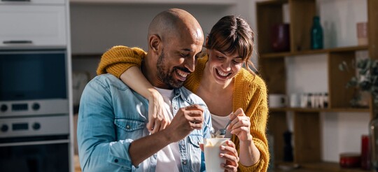 Lachendes Paar isst gemeinsam Joghurt in der Küche.