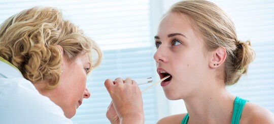 Eine Ärztin begutachtet den Rachenraum einer Patientin.