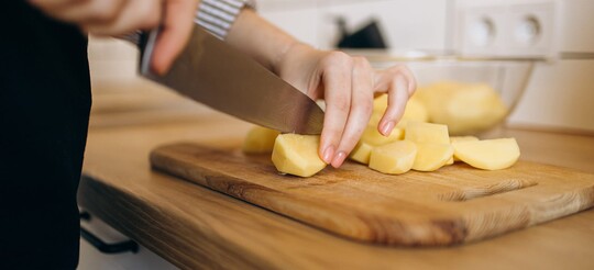 Eine Person schneidet Kartoffeln auf einem Küchenbrett als Hausmittel gegen den stillen Reflux.