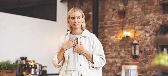 Frau schaut besorgt und fasst sich mit der Hand an die Brust.