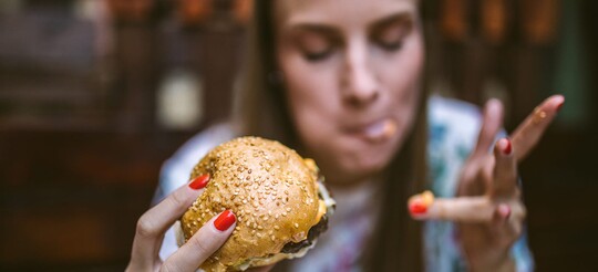 Nahaufnahme einer Frau mit Burger in der Hand, während sie sich die Finger ableckt.