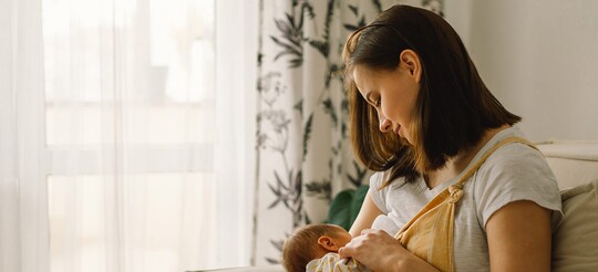 Eine Mama sitzt auf der Couch während sie ihr Neugeborenes stillt.