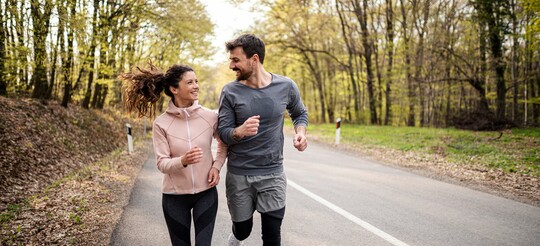 Ein lächelndes Paar beim gemeinsamen Joggen auf einer Landstraße im Wald.