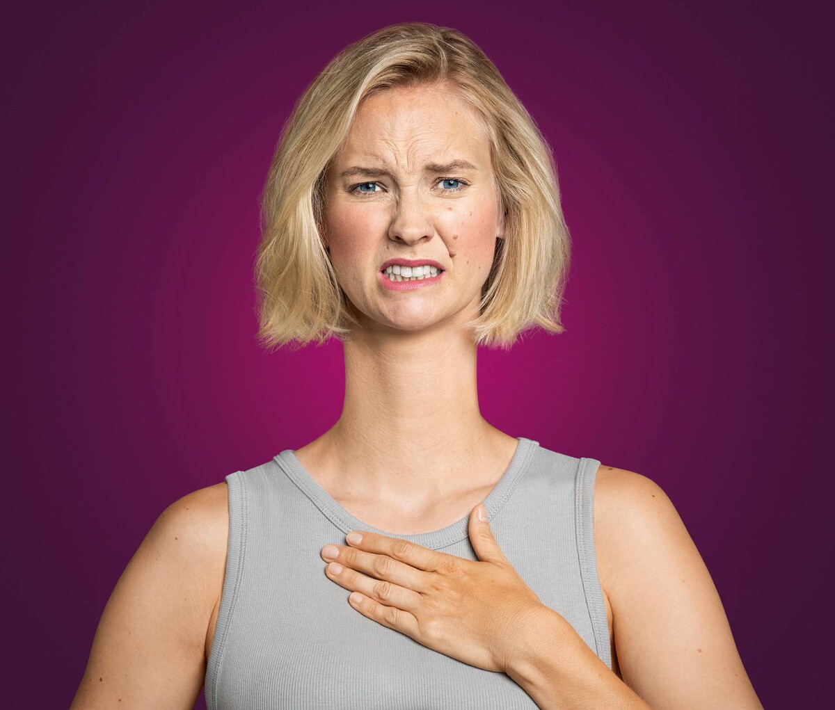 Blonde Frau mit fast schon schmerzverzerrtem Gesicht, hält sich die Hand auf die Brust. Sie hat sichtlich Probleme mit Sodbrennen