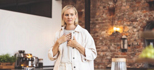 Frau schaut besorgt und fasst sich mit der Hand an die Brust.
