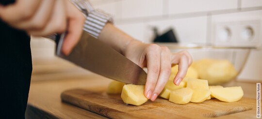 Eine Person schneidet Ingwer mit einem Messer in kleine Stücke.