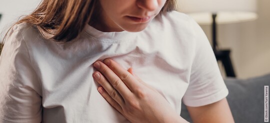 Eine Frau legt ihre Hand auf ihr Brustbein.