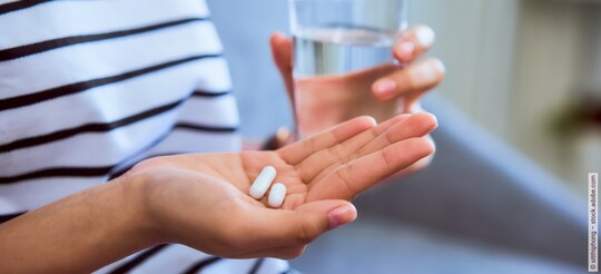 Eine Person hält zwei Tabletten und ein Glas Wasser zum Schlucken der Tabletten in den Händen.