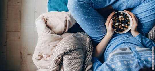 Schale mit Müsli und Beeren in den Händen einer sitzenden Person.