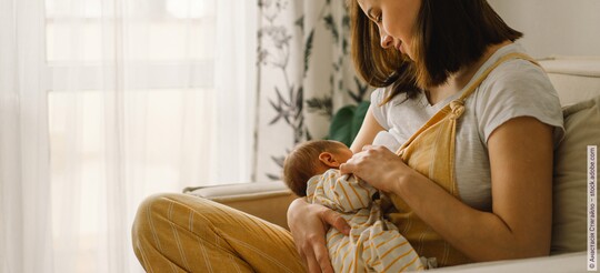 Eine Mama sitzt auf der Couch während sie ihr Neugeborenes stillt.