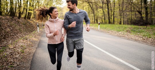 Ein lächelndes Paar beim gemeinsamen Joggen auf einer Landstraße im Wald.