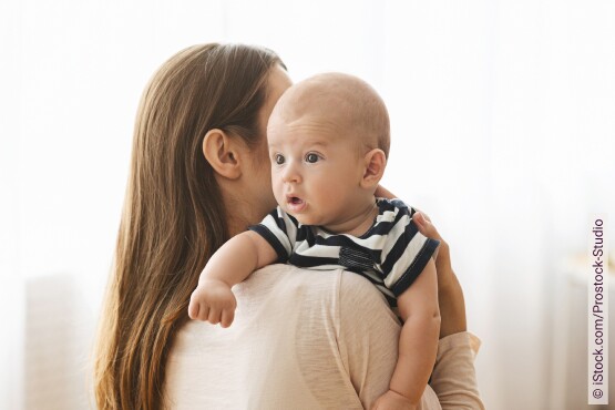 Eine Mama klopft ihrem Baby leicht auf den Rücken, damit es ein Bäuerchen macht.