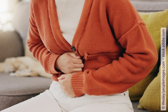 Eine Frau sitzt auf einem Sofa und hält sich nach vorn gekrümmt den Oberbauch.