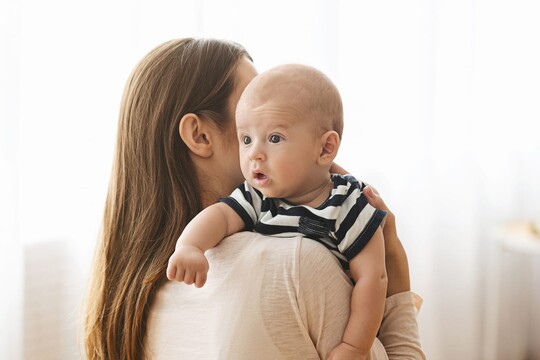 Eine Mama klopft ihrem Baby leicht auf den Rücken, damit es ein Bäuerchen macht.