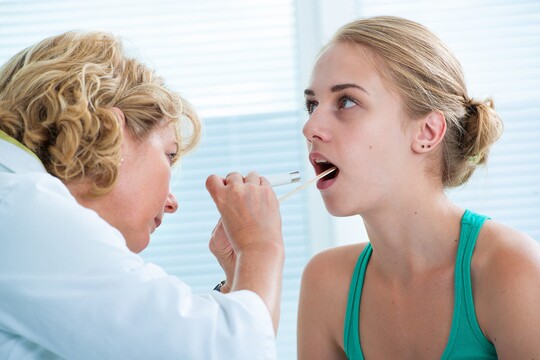 Eine Ärztin begutachtet den Rachenraum einer Patientin.