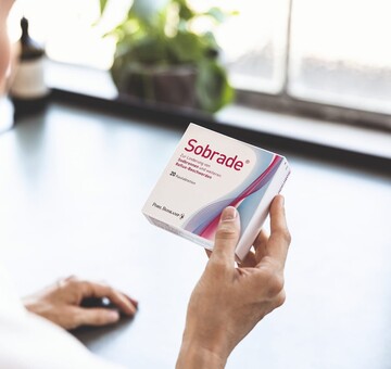 Blonde Frau ist von hinten zu sehen, wie sie eine Sobrade Verpackung mit 20 Kautabletten in der Hand hält und sich die Beschriftung durch liest