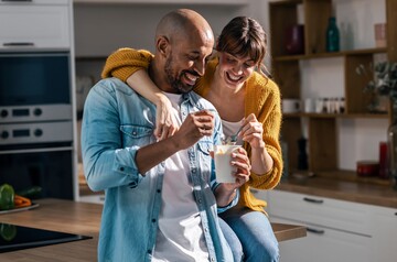 Lachendes Paar isst gemeinsam Joghurt in der Küche.